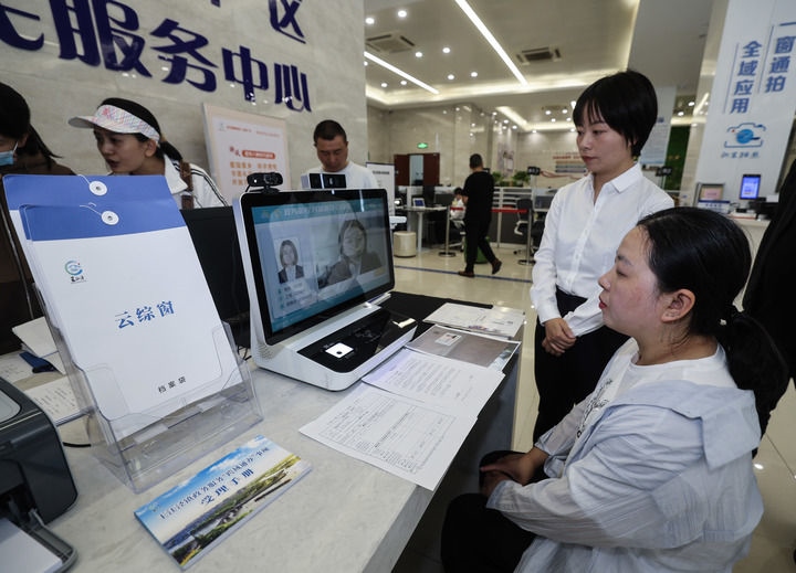 在浙江省嘉興市秀洲區(qū)王江涇鎮(zhèn)便民服務(wù)中心的“跨域通辦·云綜窗”窗口，辦理開業(yè)登記的個體工商戶（右一）通過該系統(tǒng)與江蘇省蘇州市吳江區(qū)盛澤鎮(zhèn)行政審批局工作人員視頻連線，進(jìn)行身份讀取及材料線上審核（2024年5月9日攝）。新華社記者 徐昱 攝